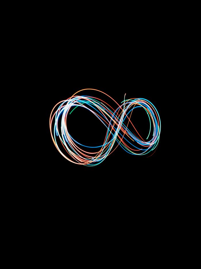 Abstract long exposure shot of colorful light trails forming an infinity symbol against a black backdrop.