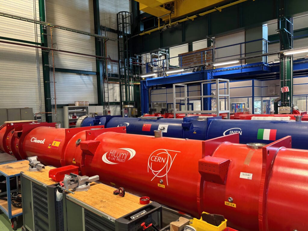 Large red and blue superconducting magnets branded with CERN and "HiLumi HL-LHC Project" logos in a technical workshop, being prepared for the High-Luminosity LHC upgrade.